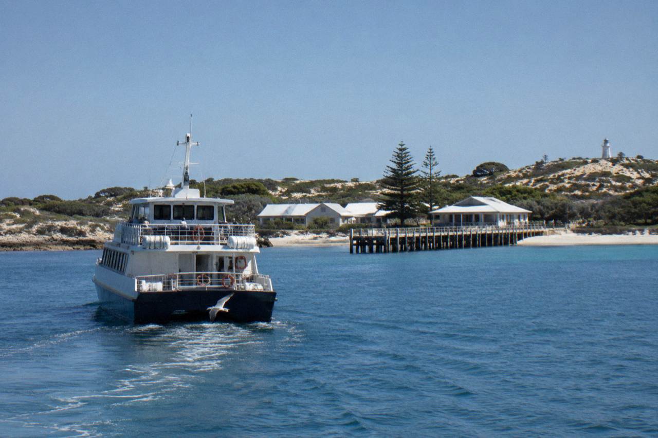 A ferry crossing calm open water toward an island coastline under a wide sky