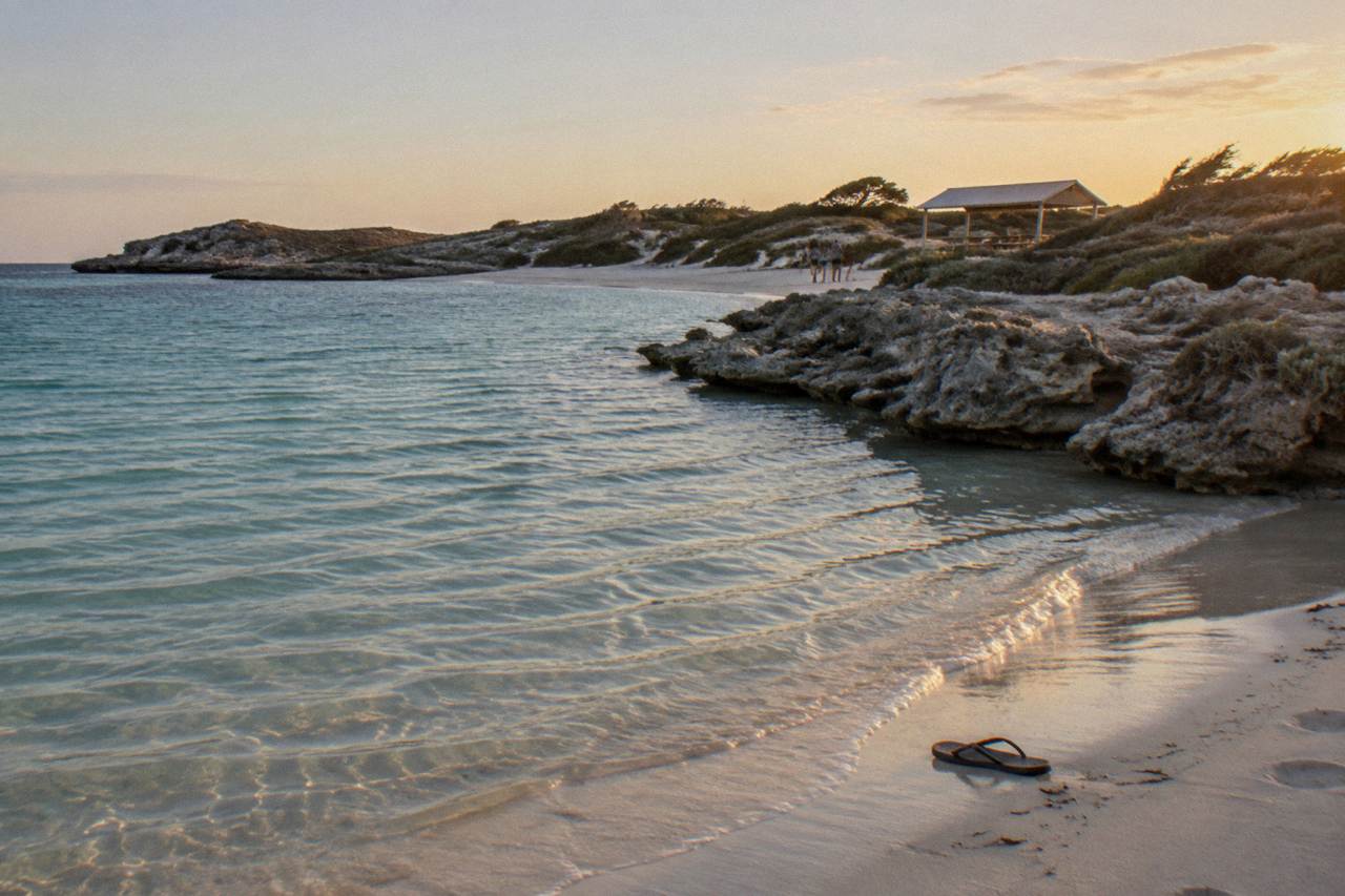 Turquoise shallow water and pale sand at a Rottnest Island bay with low coastal scrub