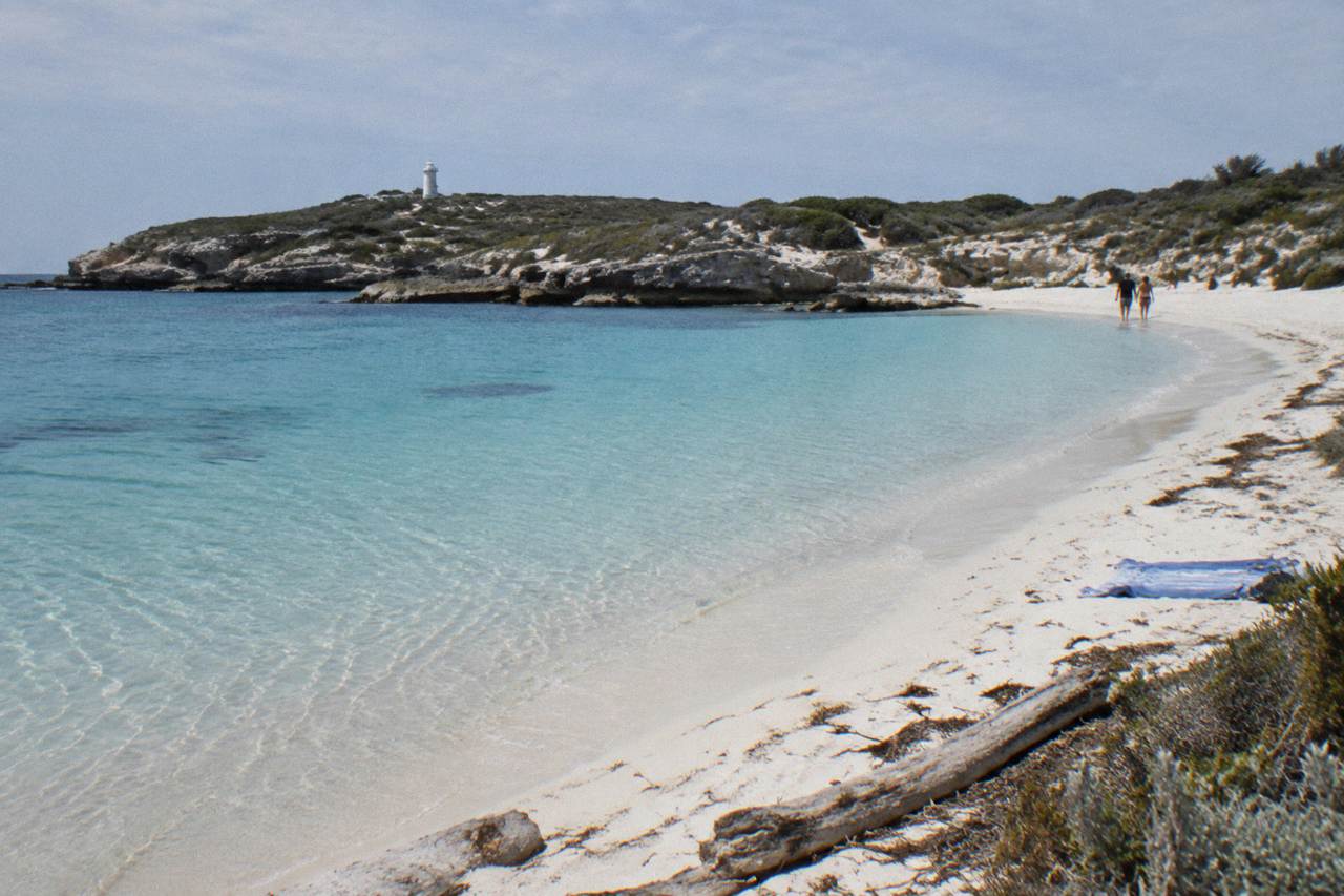 Clear turquoise water and pale sand at a sheltered Rottnest Island bay with low coastal scrub