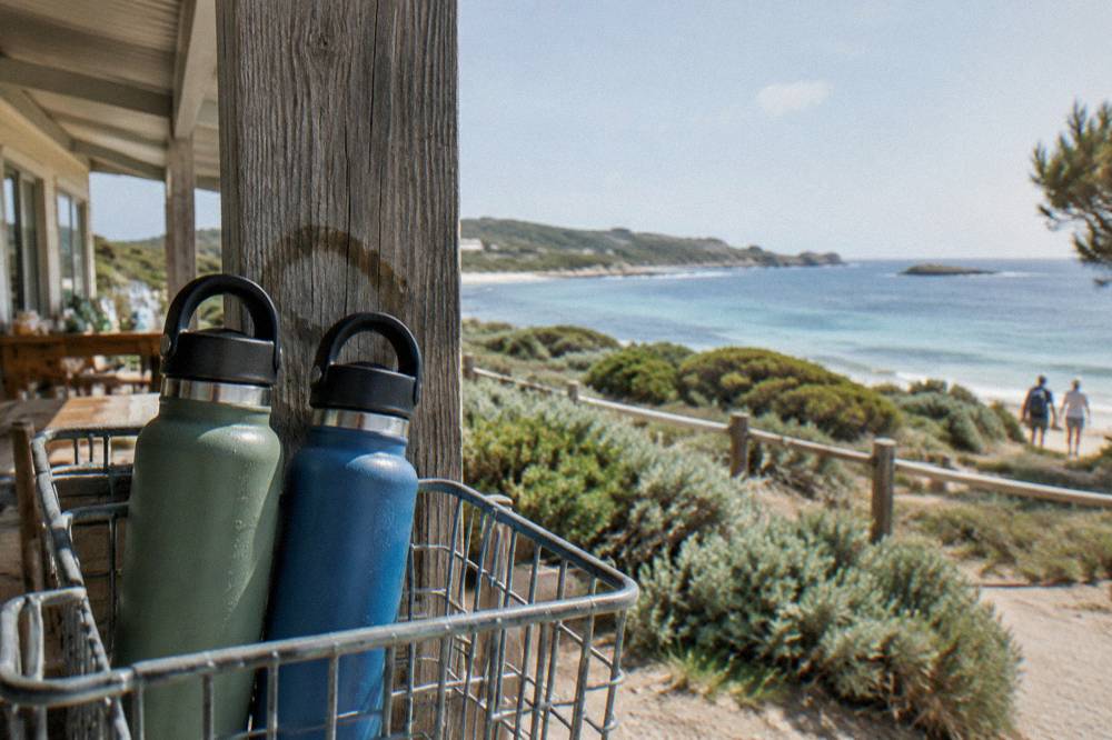 Two full reusable water bottles resting in the basket of a bicycle parked near a store verandah at Rottnest Island.