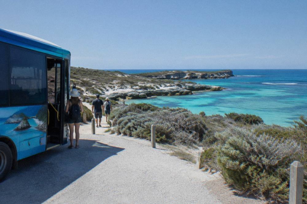 A hop-on hop-off bus stopped at a coastal lookout with turquoise water beyond
