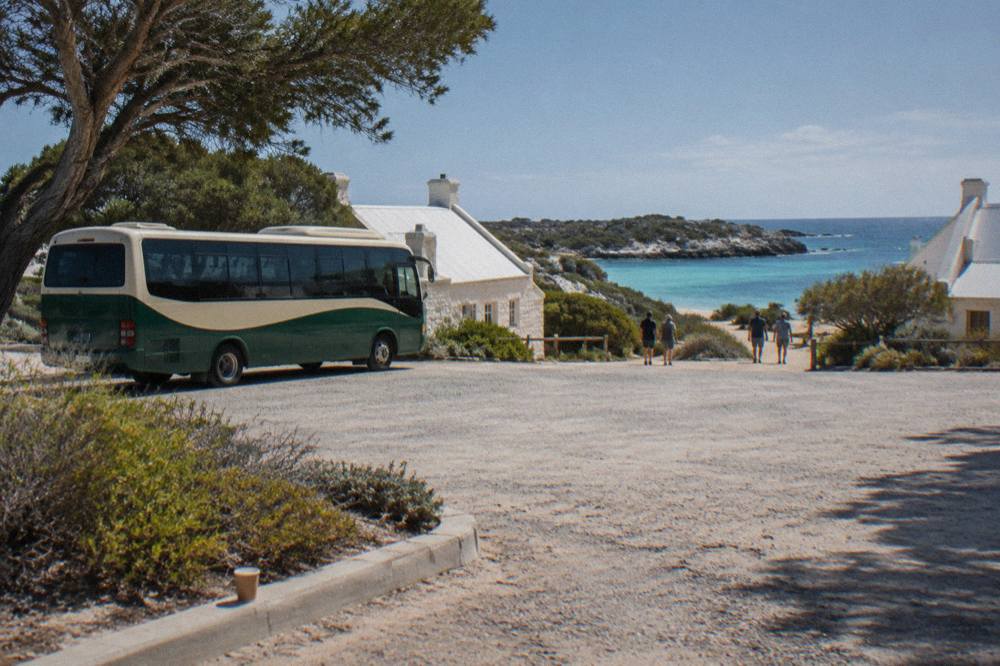 Guided tour bus parked near the Rottnest Island settlement with turquoise bay behind