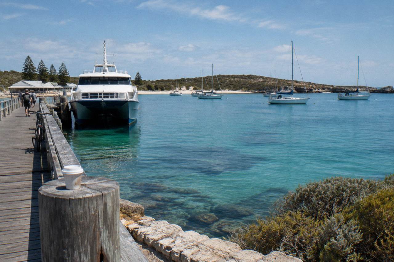 A ferry at a jetty on Rottnest Island with calm turquoise water and moored boats