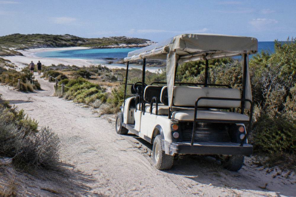 A small open electric rickshaw parked on a sandy track near coastal scrub on Rottnest Island