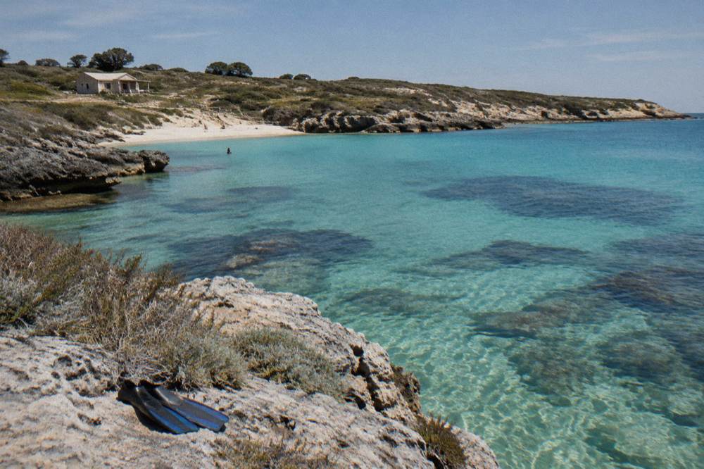 A calm swimming beach with clear water and rocky headland on Rottnest Island