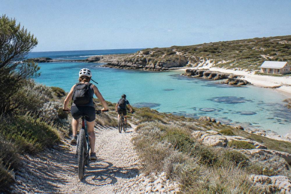 Cyclists riding along a coastal path above a turquoise bay on Rottnest Island