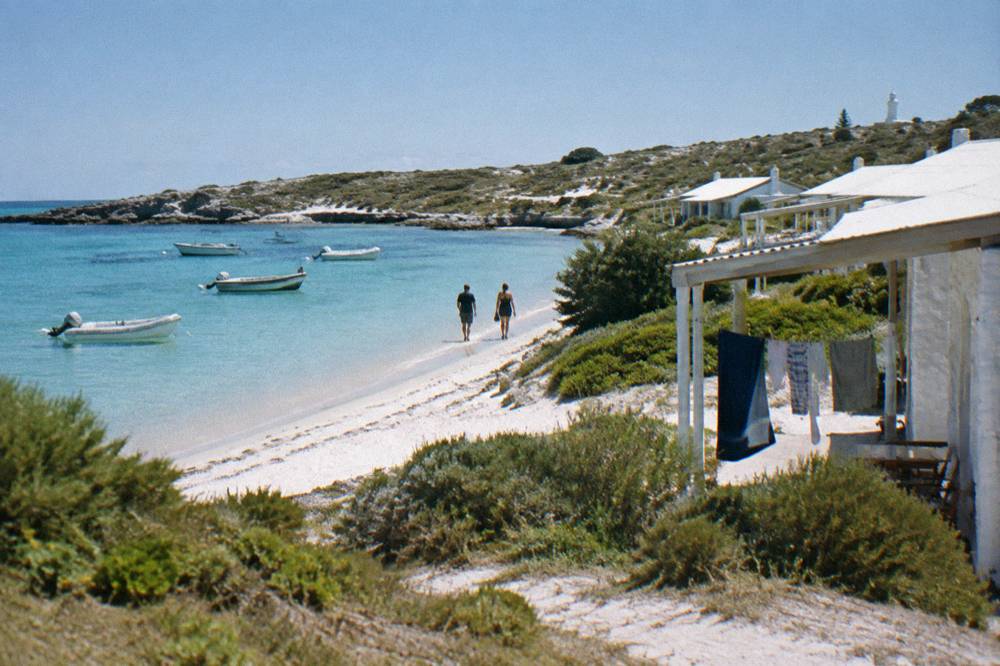 Calm turquoise bay with moored boats and low coastal buildings behind the sand