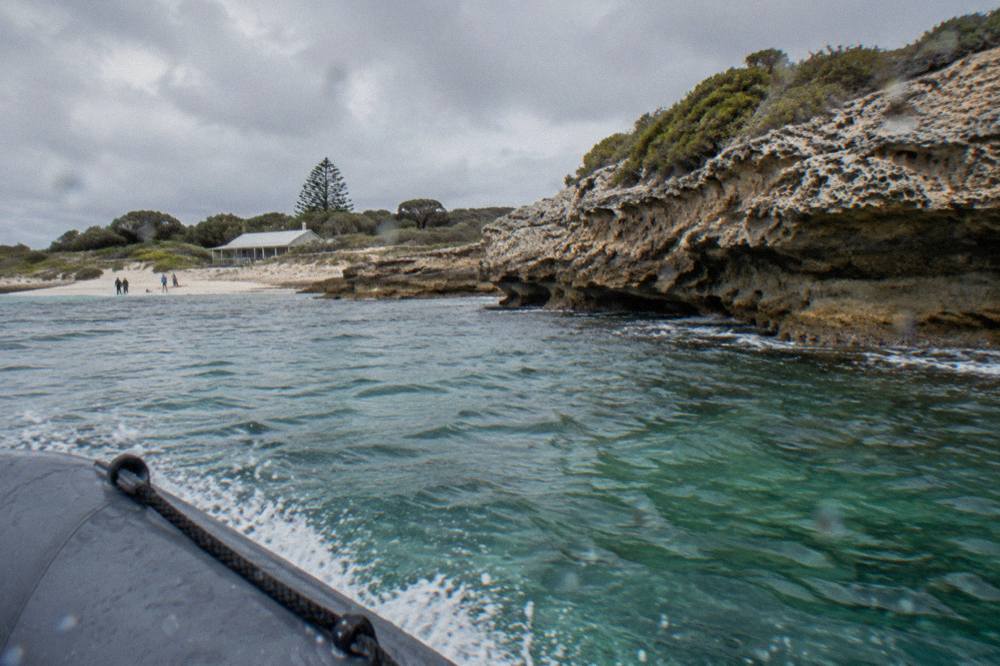 A rigid inflatable boat speeding past low limestone cliffs above clear green water