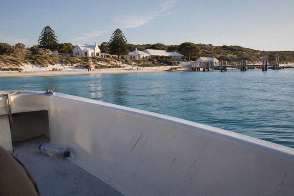 A low boat deck with the shoreline of a small island settlement across sheltered blue water