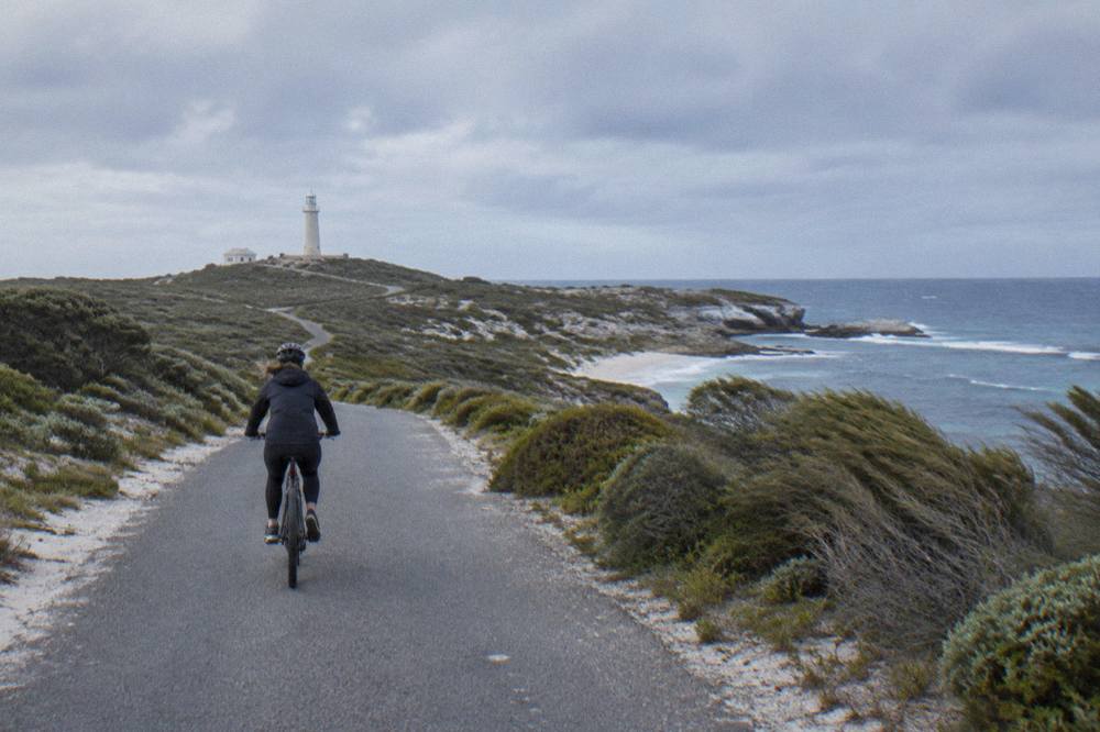 A cyclist riding a quiet sealed path beside low coastal scrub on Rottnest Island