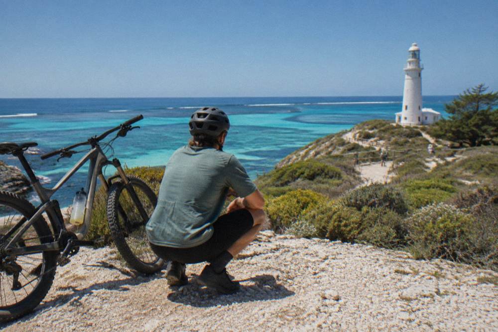 A cyclist stopped at a coastal lookout above turquoise water and limestone rocks