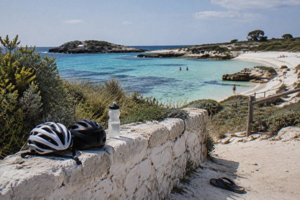 Bicycles leaning against a fence near white sand and calm shallow water
