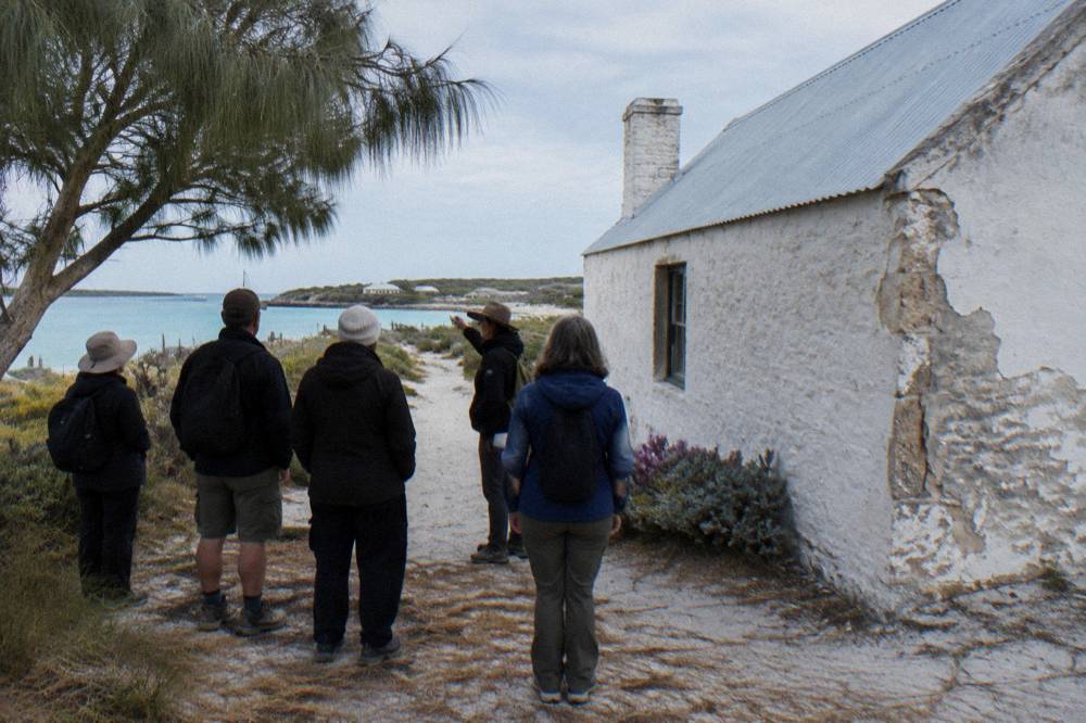 A small group of walkers with a guide standing beside a stone heritage building near the waterfront