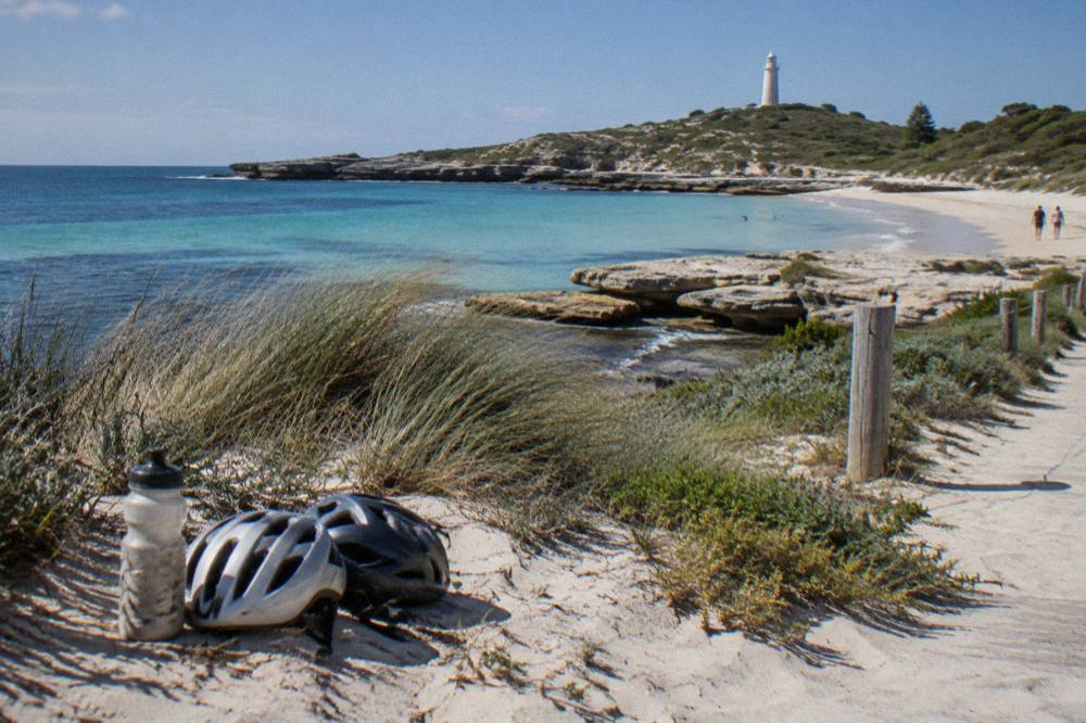 Bicycles parked on a sandy path beside turquoise water at a Rottnest Island bay