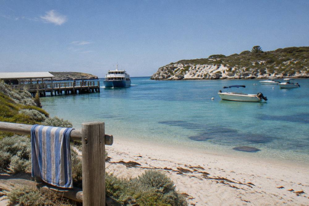 A ferry approaching the main jetty at Thomson Bay with moored boats and sandy shoreline in clear light