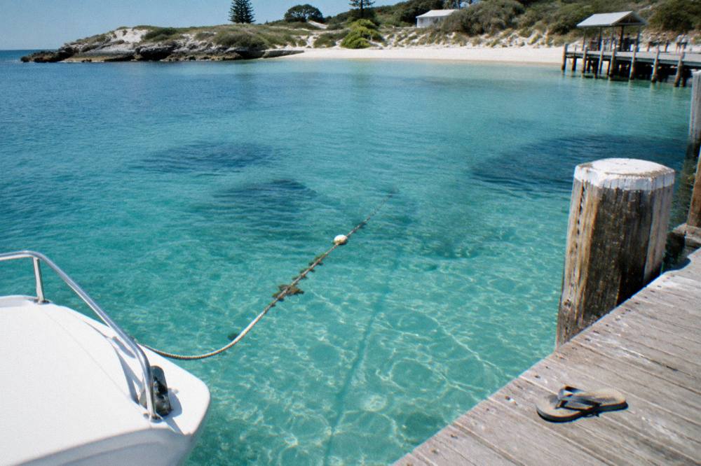 The bow of a moored ferry seen from a jetty with clear shallow water over sand below