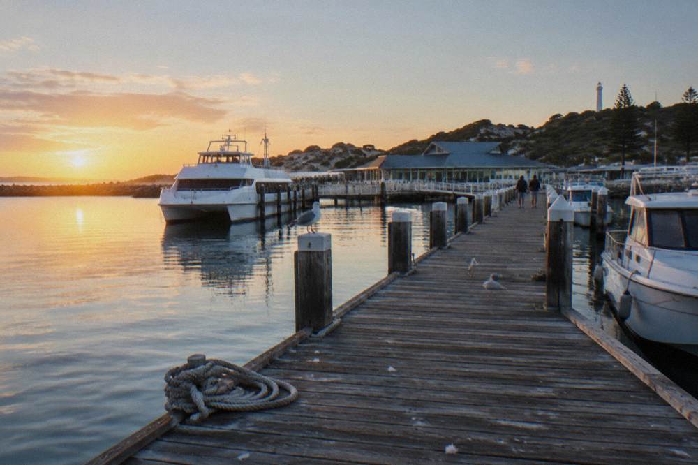 A boat harbour at sunrise with moored vessels and a jetty leading to calm open water