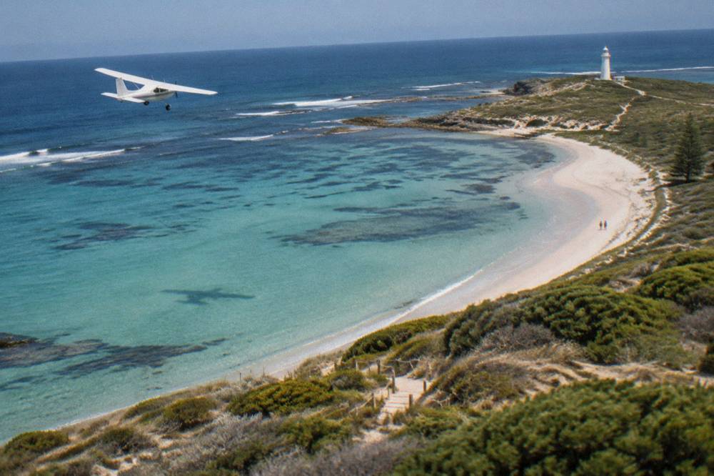 A small light aircraft flying over turquoise reef water and pale sand coastline