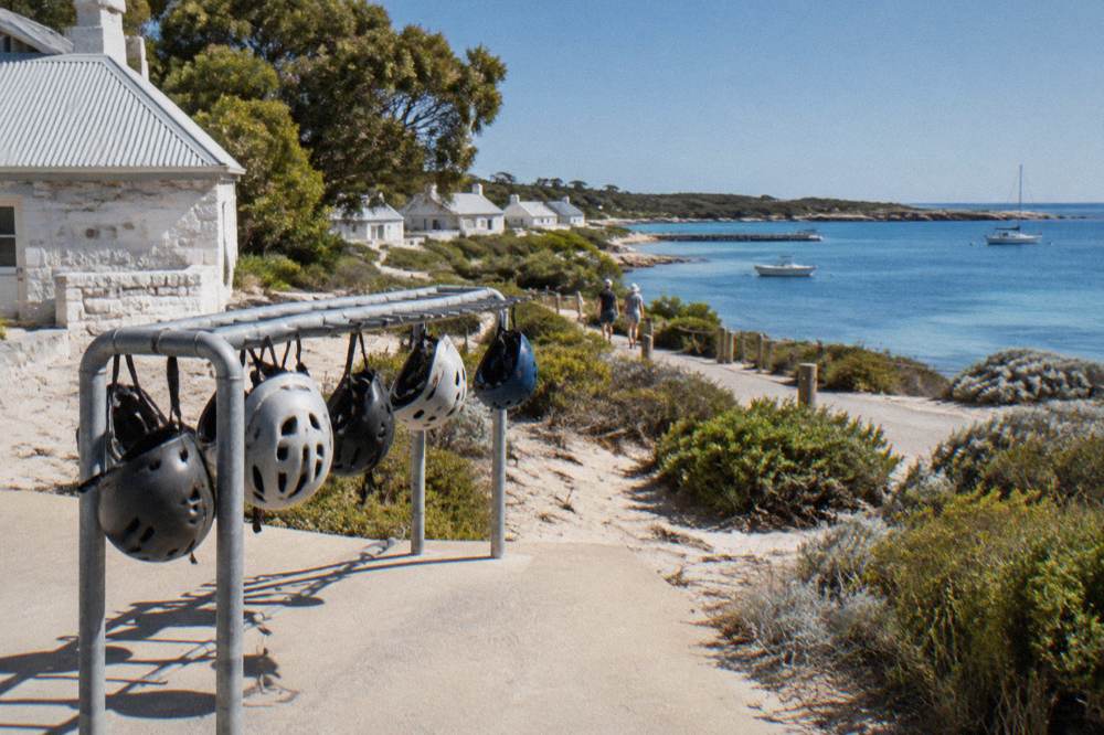 Bicycles leaning on a rack beside a coastal path with calm blue water beyond