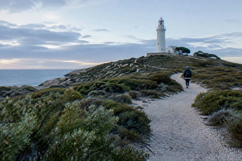 Gravel walking trail leading across low heath toward a stone lighthouse on a low rise