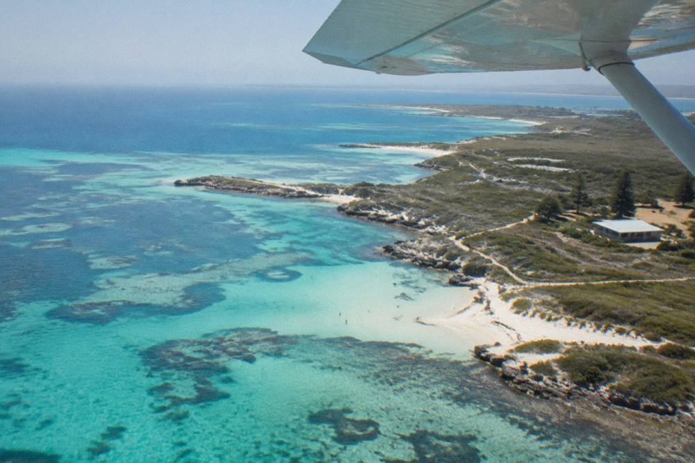 A light aircraft wing above the coastline of an island with turquoise bays.