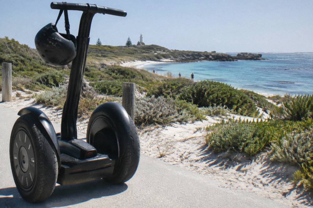 Two-wheeled segway parked on a paved path beside white sand and low dune vegetation