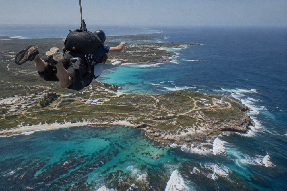 A tandem skydiver in freefall above dark blue ocean and reef outlines