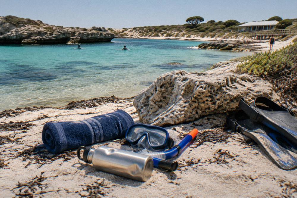 A towel, snorkel mask and water bottle laid out on sand beside a bicycle