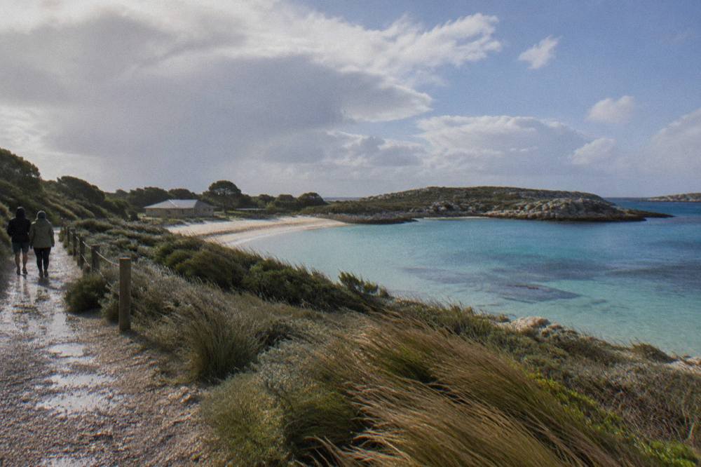 A sheltered Rottnest bay with calm clear water and low coastal scrub in warm afternoon light