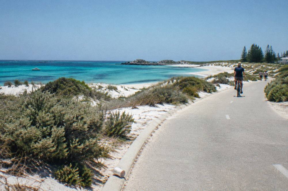 A paved coastal cycle path on Rottnest Island curving past low dunes toward the sea