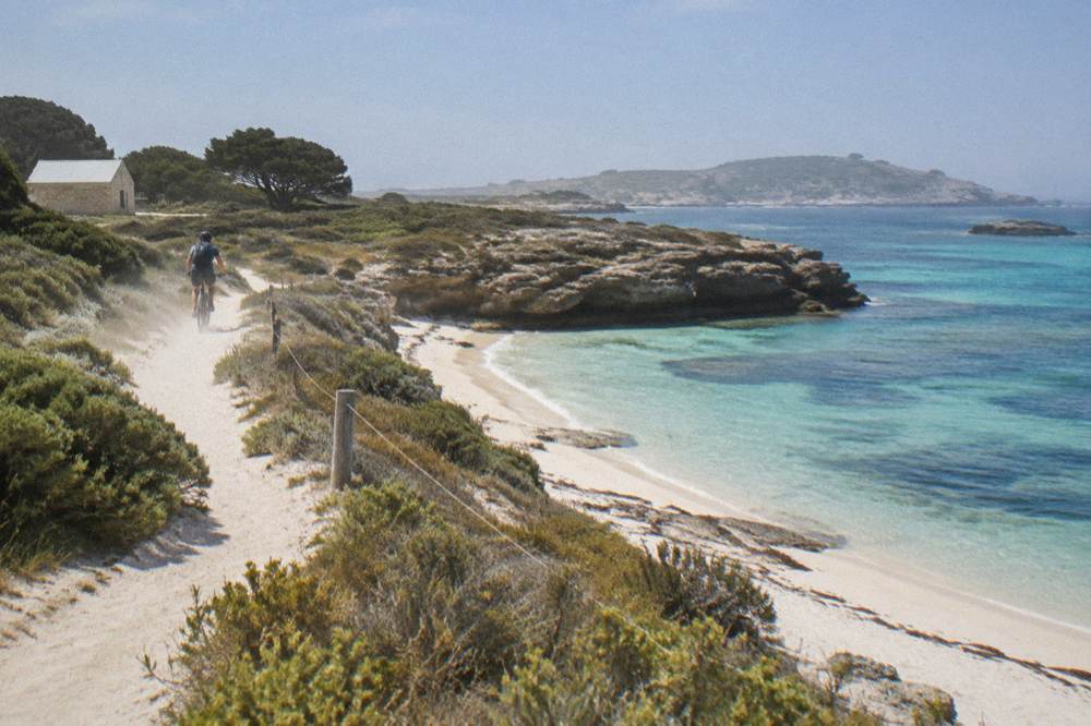 A cyclist riding a path along a coastline of pale sand and clear water