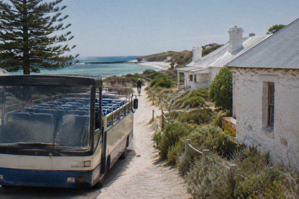 Open-top bus parked beside the Thomson Bay settlement with cyclists passing on a shared path